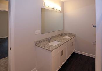 En-suite bathroom with double vanity, undermount sinks, wood-style flooring.